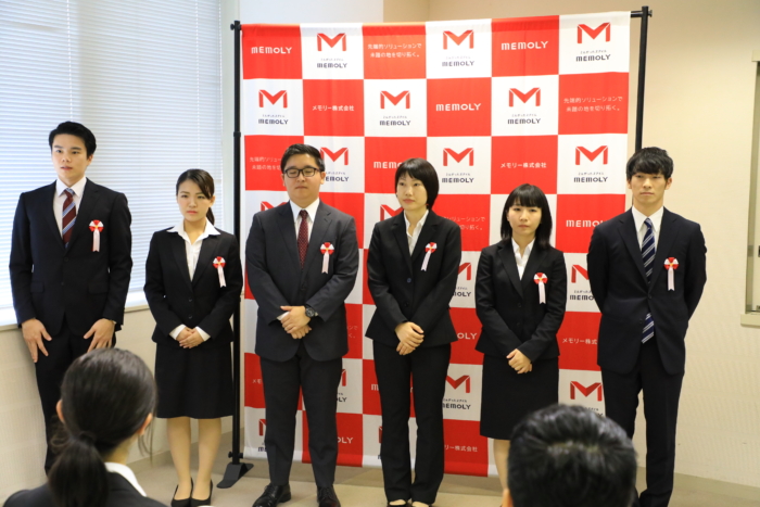 弾幕の前にスーツを着て並ぶ男女