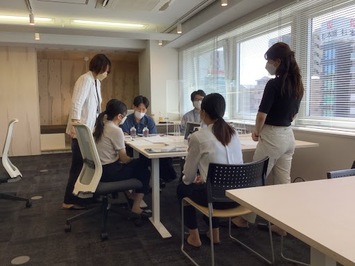 机を囲みながら学生と社員が事業立案を行っている