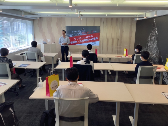 スーツを着た男性がスクリーンの前で会社説明をしている