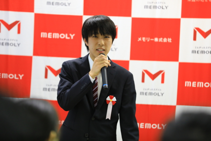 弾幕の前でぎこちなく自己紹介をする男性なお内定者