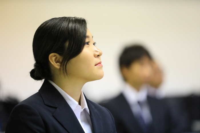 上をみて真剣に話を聞くお団子頭の女性社員