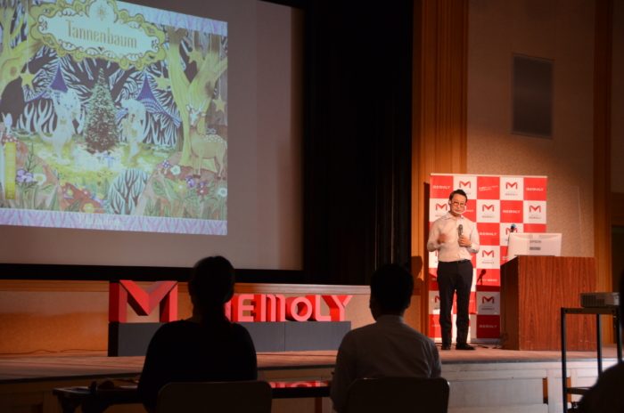 大勢に向けて熱弁する眼鏡をかけたスーツの男性