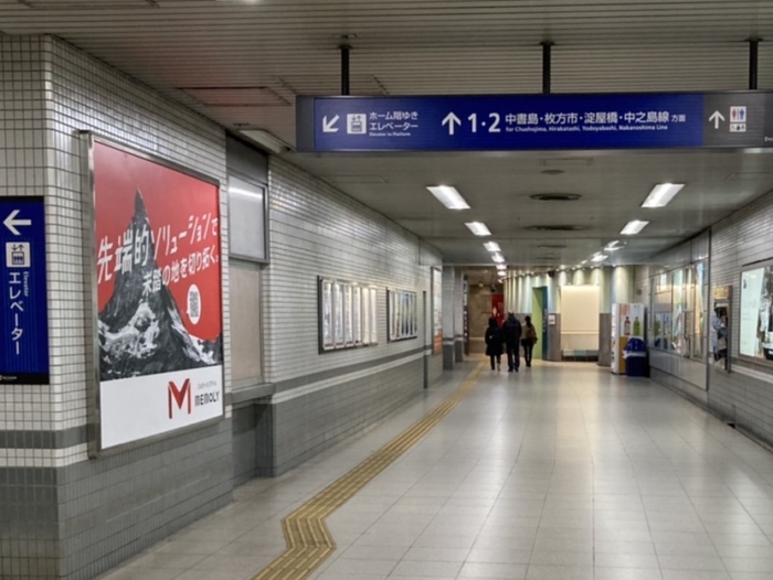 駅構内の通路にて左側の壁面に赤色の広告が設置されている