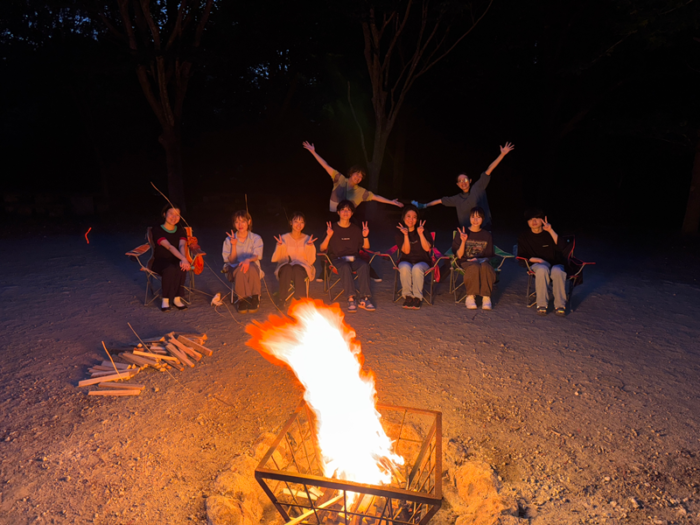 キャンプファイヤーの後ろで楽しそうにしている人たち