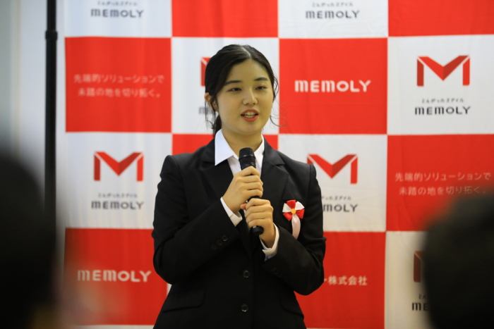 弾幕の前で笑顔かつ流暢に話す女性内定者