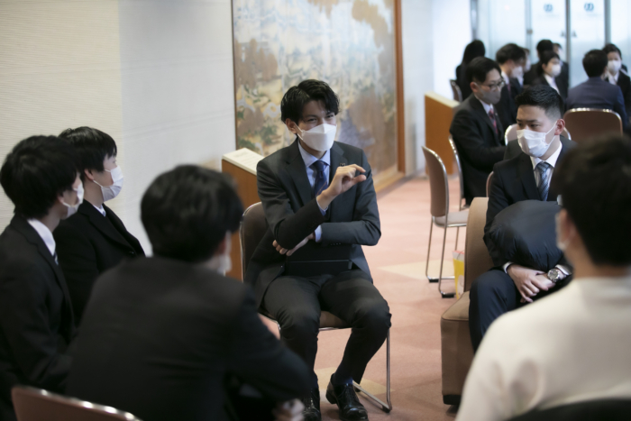 手を前に出し質問に答えるスーツの男性